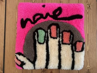 nailの文字の下に右手が描かれたラグ。ピンクのネイルの中に、人差し指だけエメラルドグリーンが混じっている。